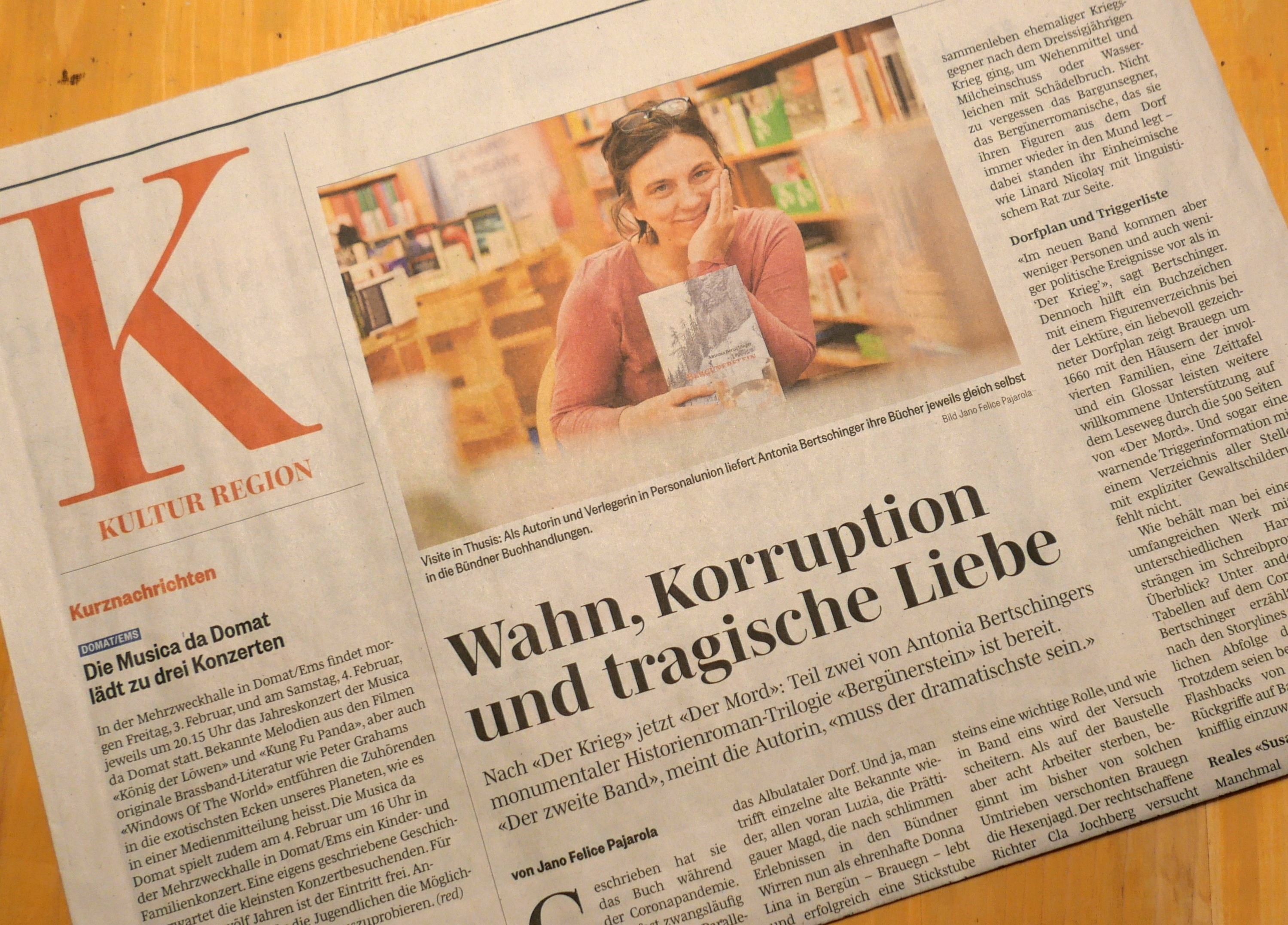Foto einer Zeitung auf einem hellbraunen Holztisch. Oben ein Bild der Autorin, sie sitzt in einer Buchhandlung und lächelt in die Kamera. Darunter die Schlagzeile "Wahn, Korruption und tragische Liebe"